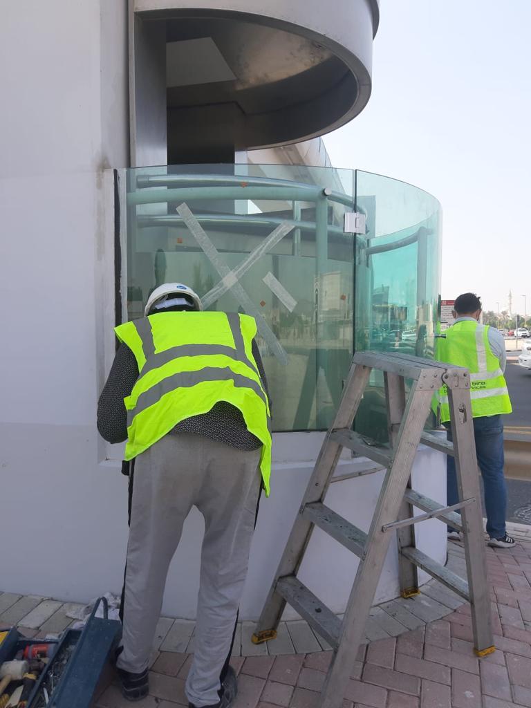 Two technicians replacing a curved glass panel on a public structure