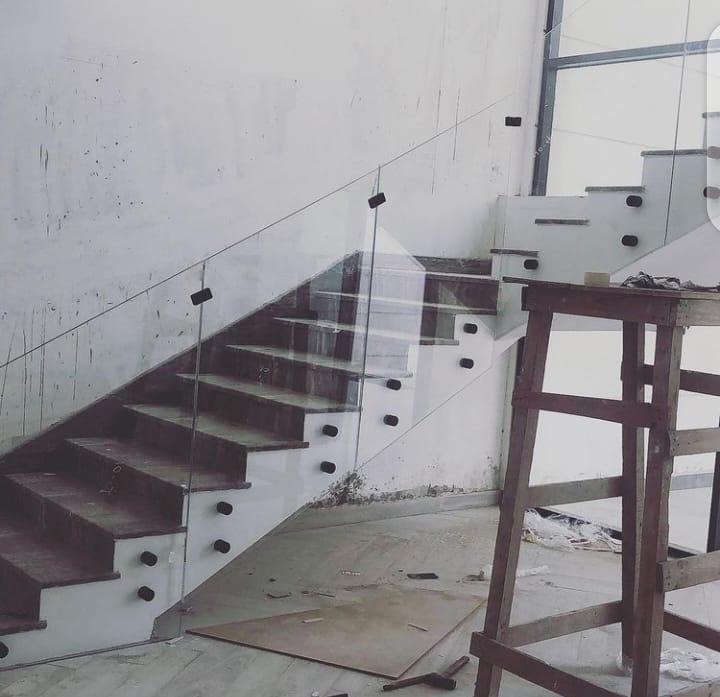 Glass staircase railing installation in progress on a bare concrete stair
