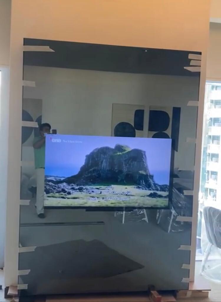 Large mirror glass wall panel being lifted into place around a TV