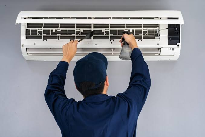 Technician deep cleaning a split AC indoor unit with coil treatment spray